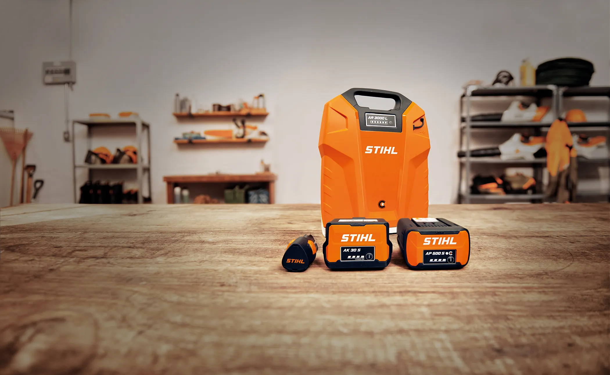 STIHL battery system components displayed on a wooden table, including backpack battery, compact batteries, and charging accessories