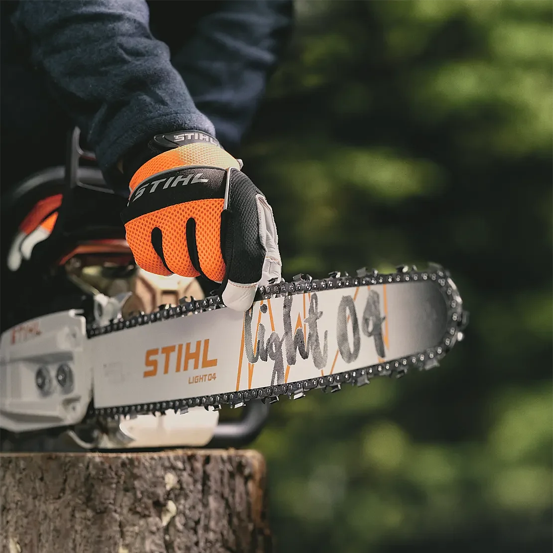 Close-up of a STIHL chainsaw guide bar and chain held by a gloved hand, highlighting cutting precision and chain detail.